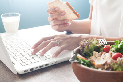 Midsection of woman using laptop with breakfast at table