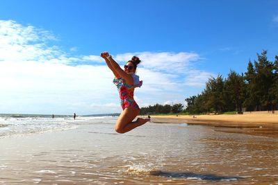 Side view of excited woman jumping at beach against sky