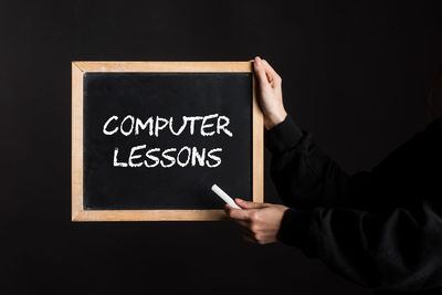 Midsection of man holding blackboard against black background