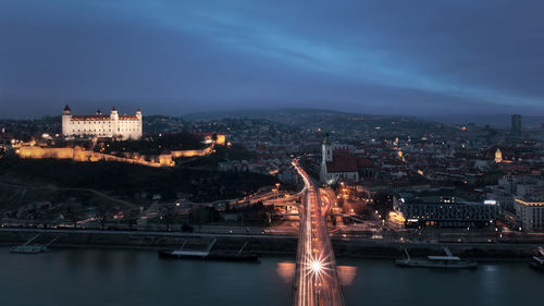 Illuminated city by river against sky