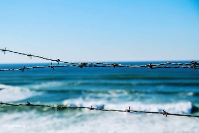 Close-up of barbed wire against sea and clear sky