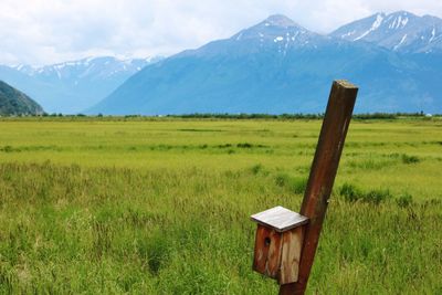 Wooden post on field by mountains against sky