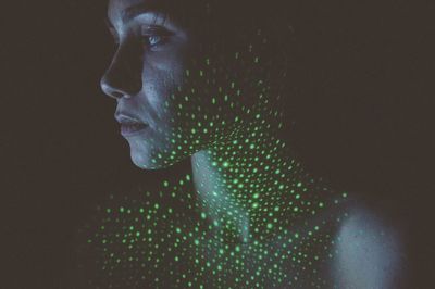 Close-up of shirtless woman with illuminated green lights against black background
