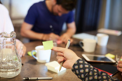 Cropped hand of businessman holding adhesive note during meeting in creative office