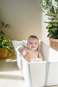 Happy smiling little baby bathing in brightly lit room among potted plants. kids having fun