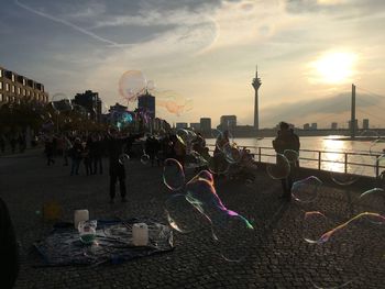 People enjoying bubbles on street with rheinturm in background during sunset