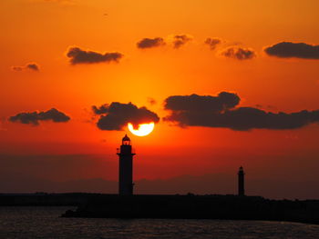 Silhouette lighthouse by sea against orange sky
