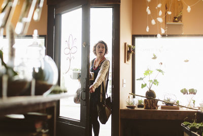 Female customer carrying plants in crate while standing at doorway of garden center