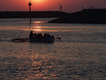 Silhouette people on boat in sea against sky during sunset