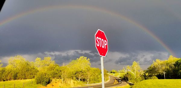 Road sign by rainbow against sky