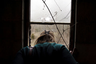 Rear view of woman looking through window at home