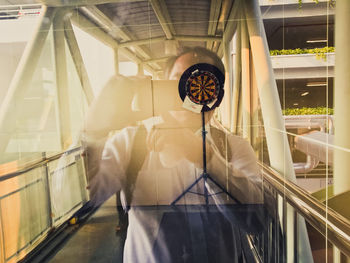 Man photographing from glass window at elevated walkway