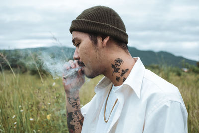 Portrait of young man smoking cigarette on field