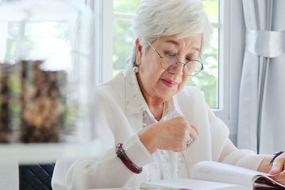 Senior woman reading book while sitting at home