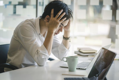 Frustrated businessman sitting with head in hands at desk in office