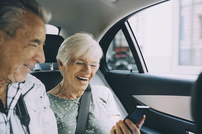 Smiling retired couple using mobile phone while sitting in car during vacation