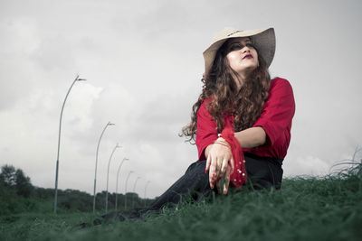 Woman wearing hat sitting on field against sky