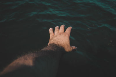 Cropped image of hand reaching towards sea