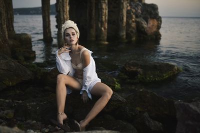 Portrait of young woman sitting on rock by sea