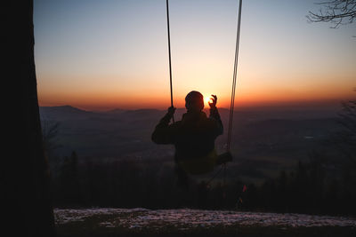 Rear view of man sitting on mountain against orange sky