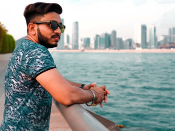 Young man wearing sunglasses against sky in city