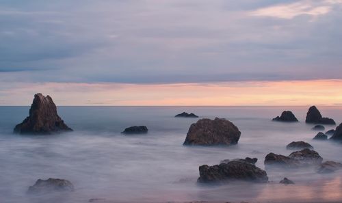 Rocks in sea against sky during sunset