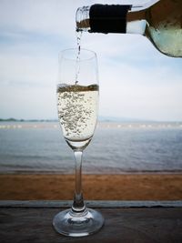 Pouring wine into a glass on table by sea against sky