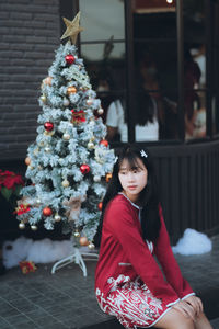 Young woman sitting against christmas tree