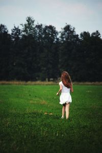 Rear view of girl running on grassy field against trees