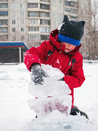 Caucasian boy in a red jacket in winter plays with ice floes in the city.