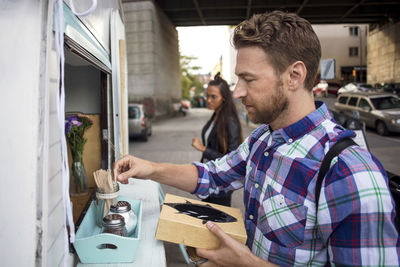 Male customer removing fork from container outside food truck with woman in background