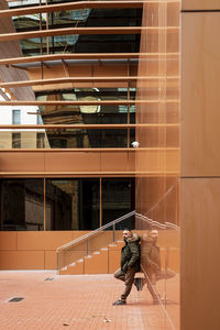 Side view of a bearded male leaning on a office building wall