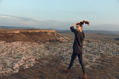 Side view of woman standing on mountain against sky