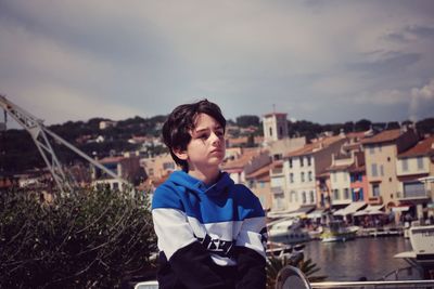 Thoughtful boy sitting in city against sky