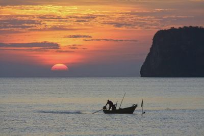 Silhouette man rowing boat on sea against sky during sunset