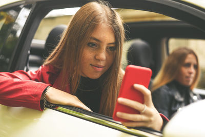 Trendy girl sitting in a car. smiling teen using smartphone chat with friend woman enjoy free time