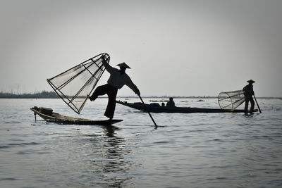 Silhouette fishermen fishing in sea against sky