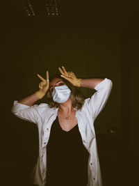 Young woman wearing mask standing against black background