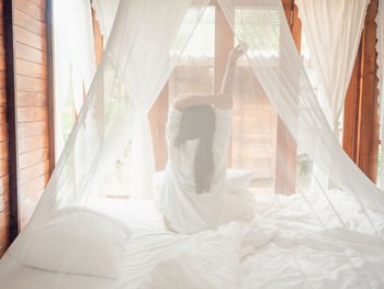 Backside of woman stretching in bed after wake up, happy greets new day with warm sunlight.