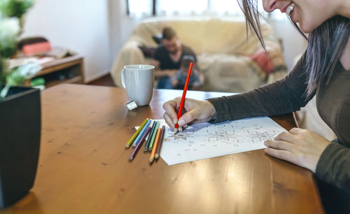 Close-up of woman drawing on paper with family in background at home