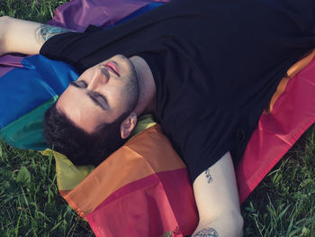 High angle view of man lying on rainbow flag at grassy field