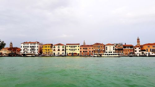 View of buildings by sea against cloudy sky