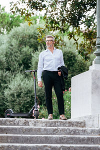 Full length of businessman with electric scooter standing outdoors