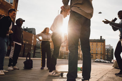 Low angle view of happy friends looking at man playing with skateboard in city