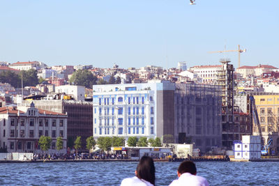 Rear view of people on river against buildings in city