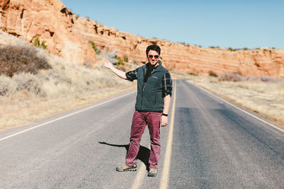 Full length of smiling man gesturing while standing on road by rock formations