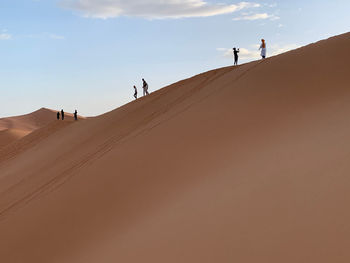 People on sand dune in desert against sky