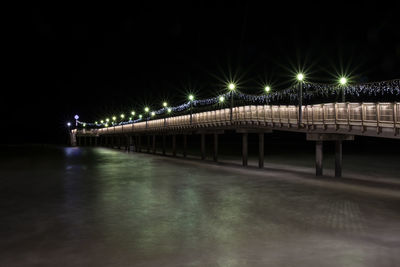 Illuminated bridge over river against sky at night