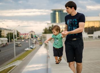 Father holding son while walking on retaining wall