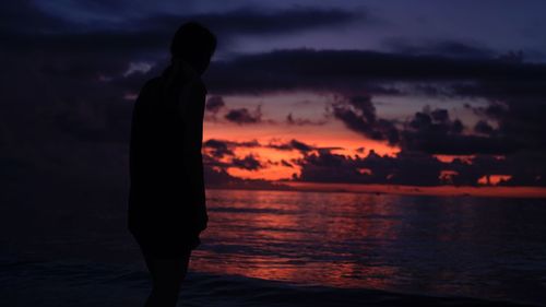 Silhouette woman standing at beach against sky during sunset